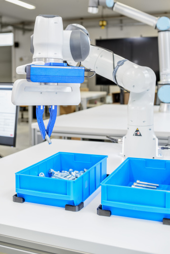 A robotic arm with Ensenso cameras grips a screw from a blue container.