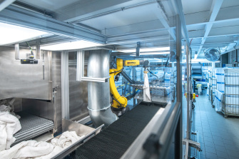 A conveyor belt with laundry and a robot unfolding the laundry in a industrial laundry.