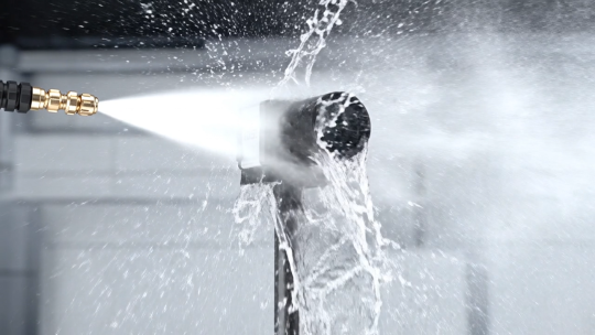 An industrial camera is sprayed with a powerful jet of water from a short distance.