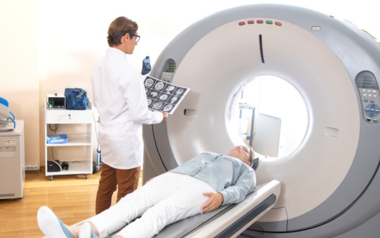 Doctor with brain scans next to MRI machine and patient lying down.