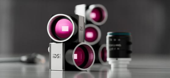 uEye CP cameras stacked, a lens next to them, grey, reflective background