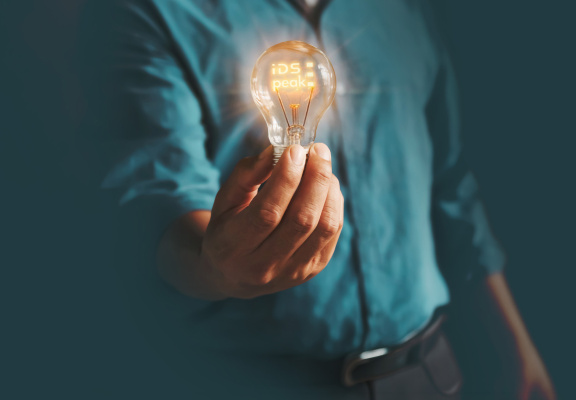 Person holding illuminated “iDS peak” light bulb against dark background