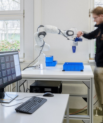 A man stands to the right of a robotic arm and reaches for the attached Ensenso camera